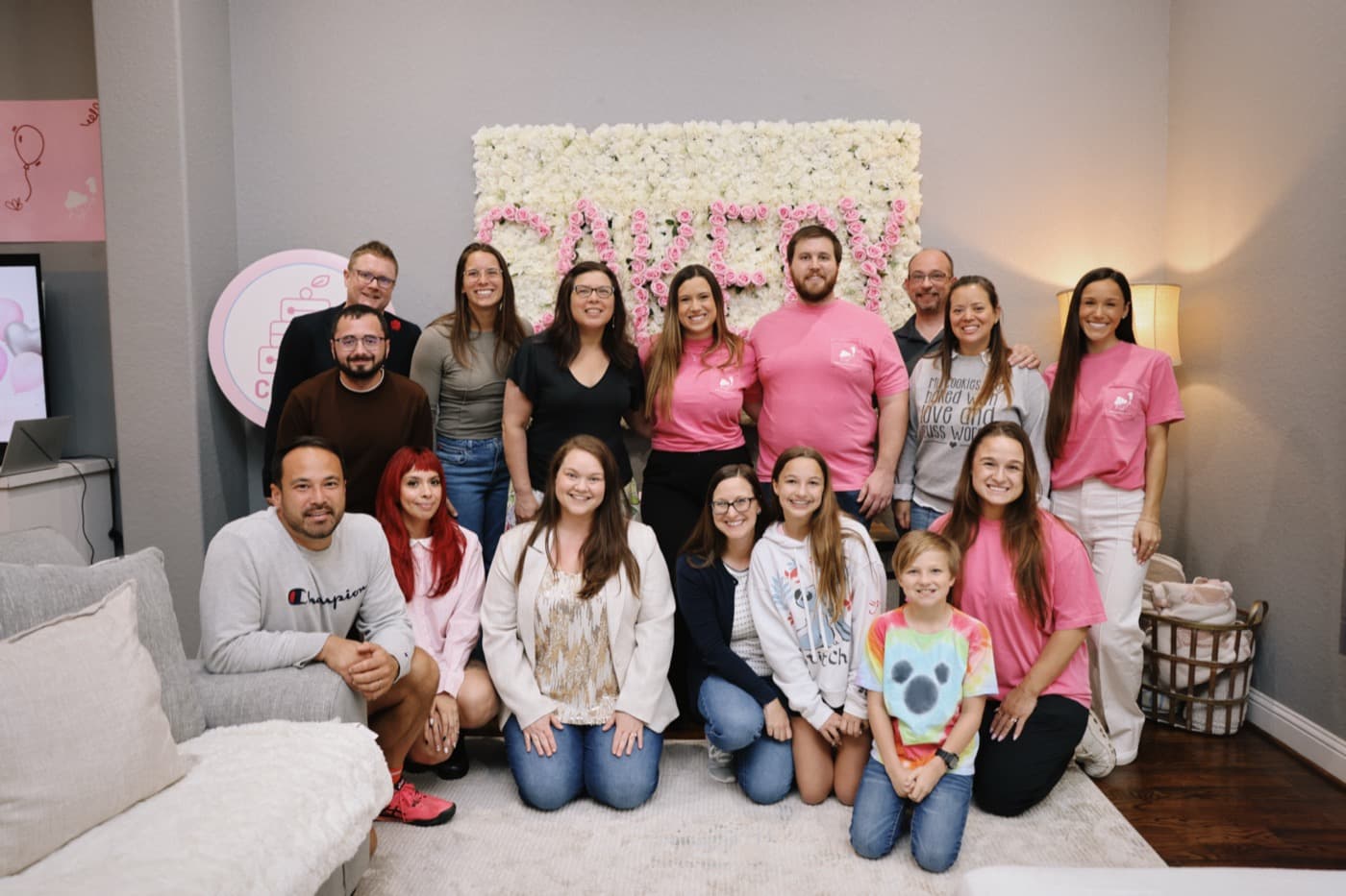 The Cakery team and bakers gathered in front of a flower wall at Cakery's one year birthday party